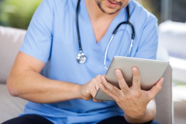 Erkek bakıcı kanepede otururken tablet bilgisayar kullanarak