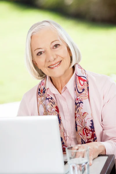 Mulher sênior feliz com laptop no alpendre da casa de repouso — Fotografia de Stock