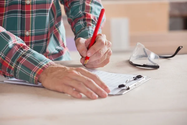 Carpintero escribiendo notas en portapapeles en la mesa — Foto de Stock