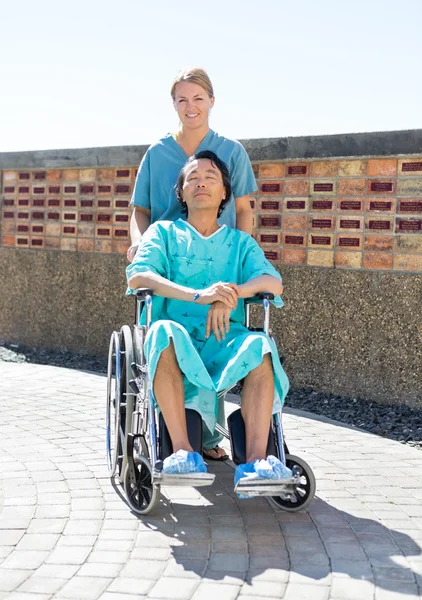 Krankenschwester schiebt entspannte Patientin im Rollstuhl in Hof — Stockfoto