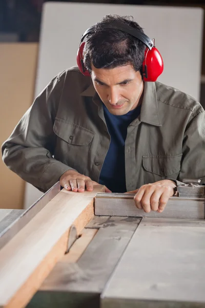 Carpinteiro masculino que corta a prancha de madeira com tabela — Fotografia de Stock