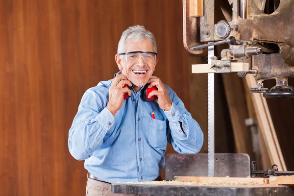Happy Carpenter drží sluchu pásové pily — Stock fotografie