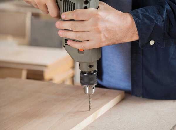 Carpenter Using Drill On Wood In Workshop