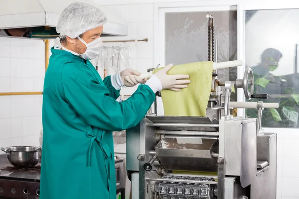 Koch wickelt grüne Nudelblätter auf Nudelholz in Maschine — Stockfoto