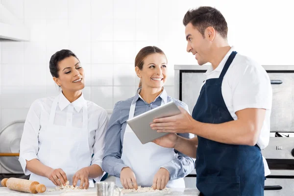 Chefs felizes discutindo receita no tablet digital na cozinha — Fotografia de Stock