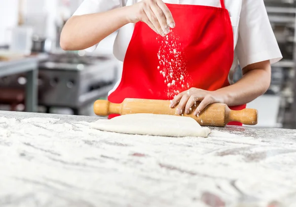 Chef polvilhando farinha enquanto rolando massa em contador bagunçado — Fotografia de Stock