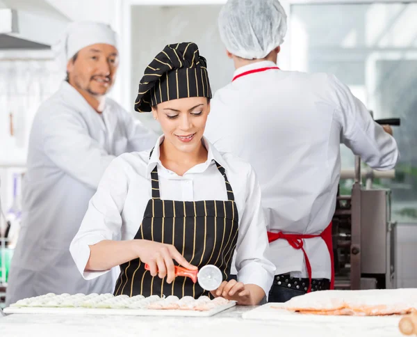 Schöne Köchin schneidet Ravioli-Pasta mit Kollegen im Hintergrund — Stockfoto