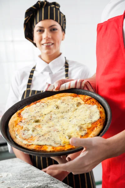 Sorridente chef in piedi da collega mostrando deliziosa pizza — Foto Stock