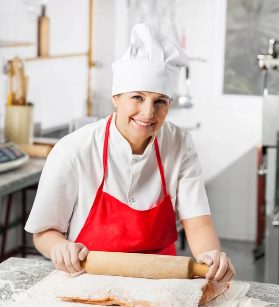 Chef femenino sonriente que rueda la hoja de pasta en el mostrador —  Fotos de Stock