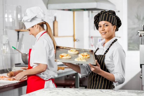 Chef feliz sosteniendo pequeñas pizzas en bandeja en la cocina —  Fotos de Stock