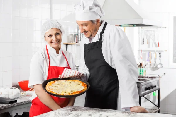 Chef heureux debout près de collègue tenant la casserole de pizza — Photo