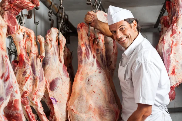 Carnicero parado junto a la carne colgado en el matadero —  Fotos de Stock