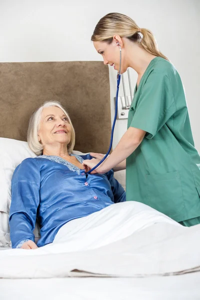 Pečovatel zkoumání starší žena s stetoskop v ložnici — Stock fotografie