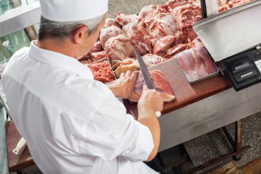 Male Butcher Cutting Meat At Display Cabinet clipart