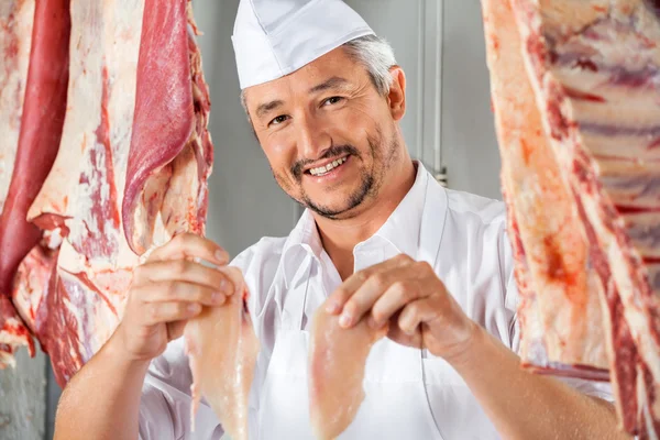 Carniceiro mostrando pedaços de frango em meio a carne — Fotografia de Stock