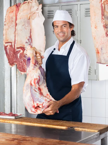 Carniceiro sorridente segurando carne — Fotografia de Stock