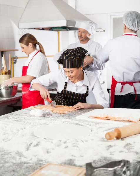 Chef corte Ravioli Pasta com colegas no fundo — Fotografia de Stock