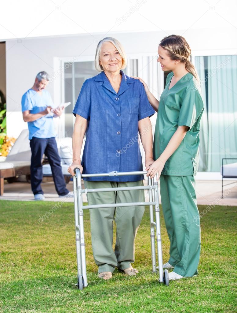 Nurse Helping Senior Woman To Use Walking Frame In Lawn