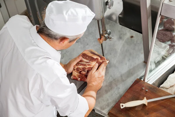 Carniceiro maduro cortando carne fresca com serra de fita — Fotografia de Stock