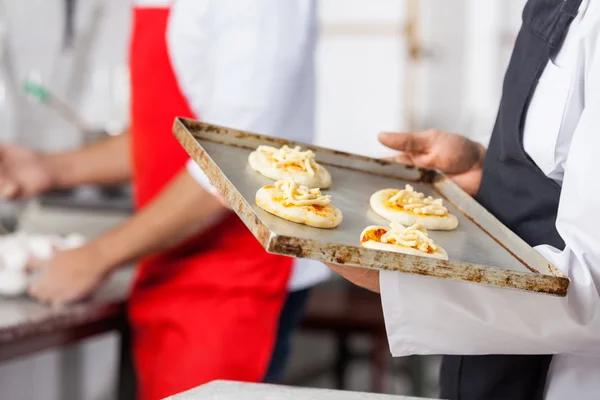 Chef che tiene piccole pizze sul foglio di cottura in cucina — Foto Stock