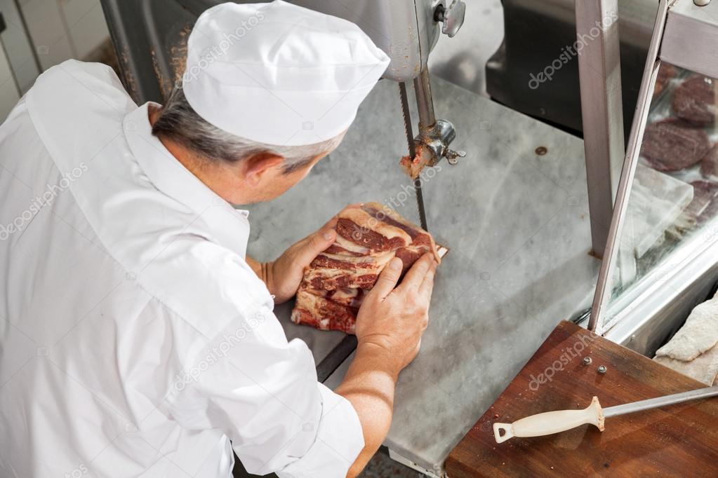 Mature Butcher Cutting Fresh Meat With Bandsaw