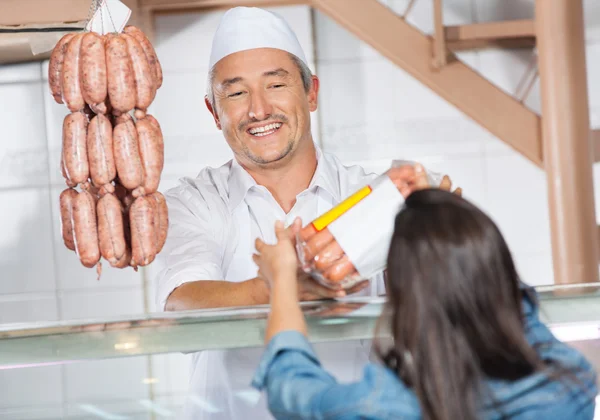 Carnicero dando salchichas empaquetadas a cliente femenino —  Fotos de Stock