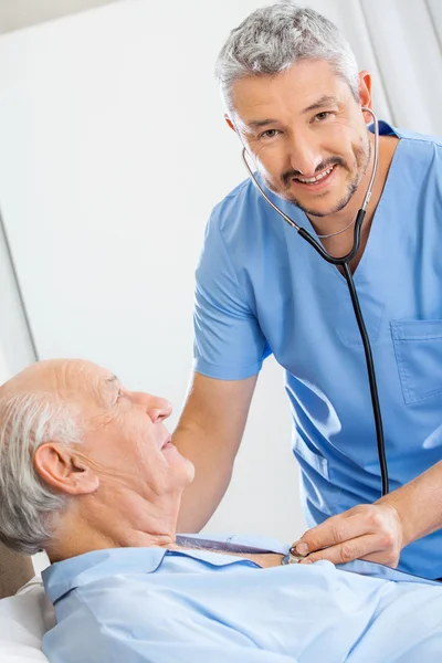 Glücklicher Hausmeister untersucht Senior mit Stethoskop — Stockfoto