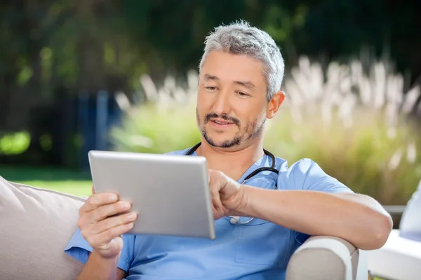 Médico masculino usando tablet digital enquanto sentado no sofá — Fotografia de Stock