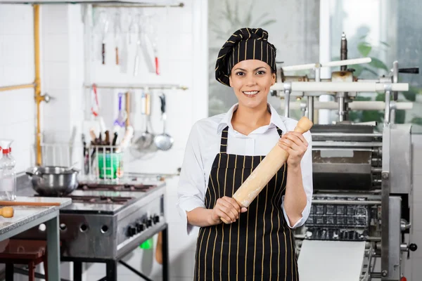 Счастливый повар женского пола, держащий скалку в кухне — стоковое фото
