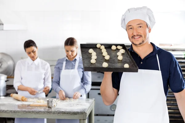 Chef sonriente llevando una bandeja para hornear con bolas de masa en la cocina — Foto de Stock
