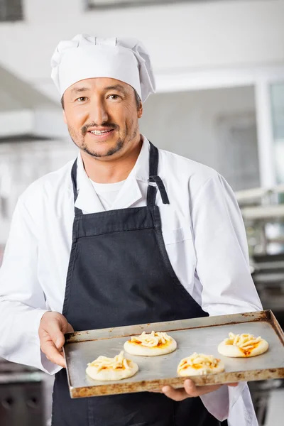 Chef confiante segurando pequenas pizzas na assadeira na cozinha — Fotografia de Stock