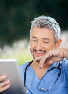 Tablet bilgisayarda bakarken gülümseyen erkek doktor