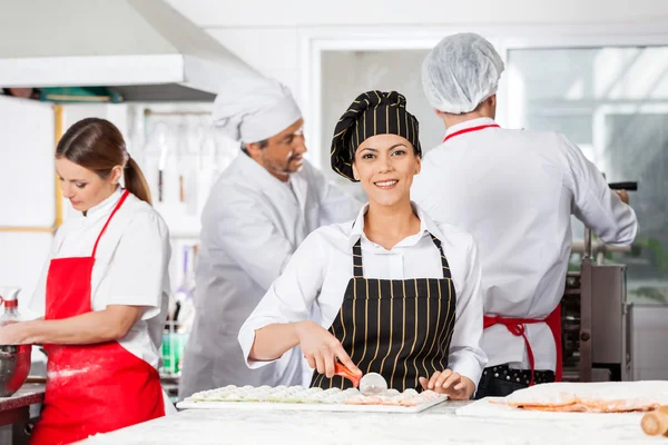 Sorrindo Chef corte Ravioli Pasta com colegas no fundo — Fotografia de Stock
