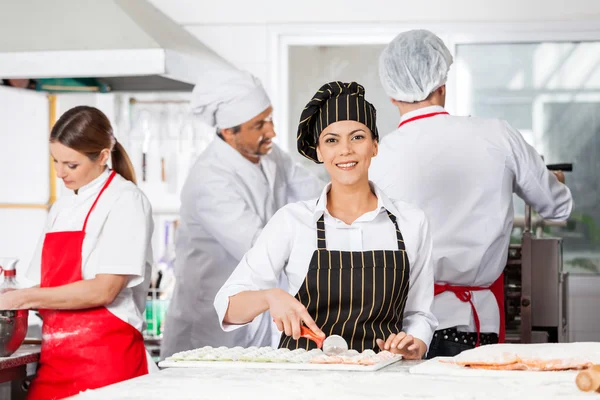 Chef souriant coupant des pâtes Ravioli avec des collègues en arrière-plan — Photo