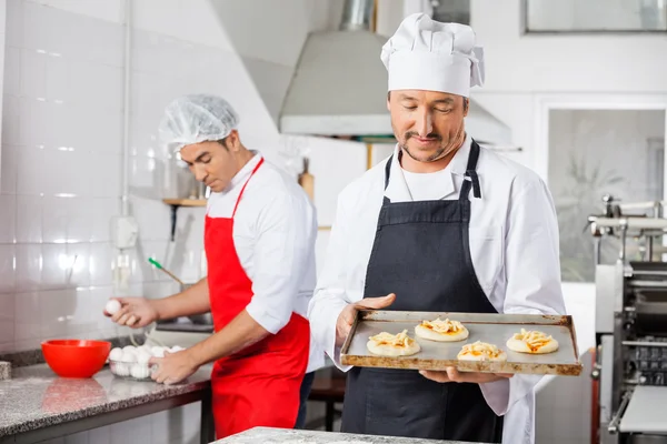 Chef sosteniendo pequeñas pizzas en bandeja con su colega en segundo plano — Foto de Stock