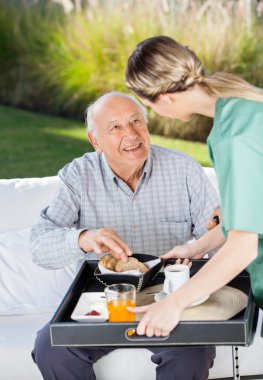 Female Caretaker Serving Breakfast To Senior Man clipart