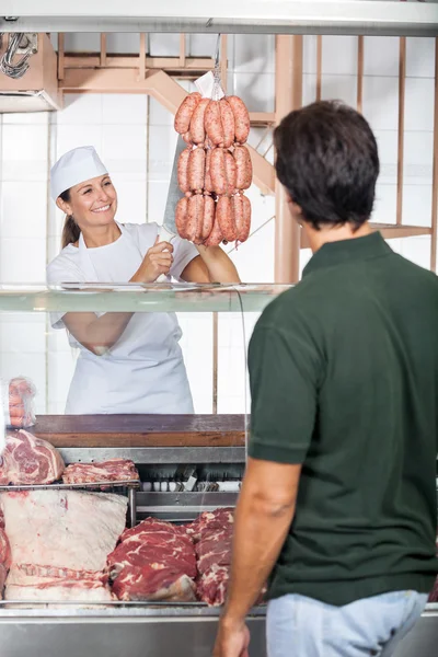 Мясник продает колбасы покупателю в магазине — стоковое фото