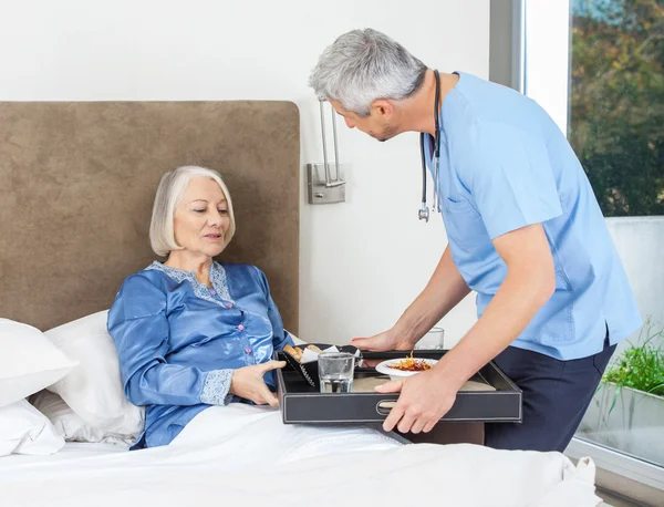 Verpleegkundige serveren van het ontbijt met Senior vrouw op Bed — Stockfoto