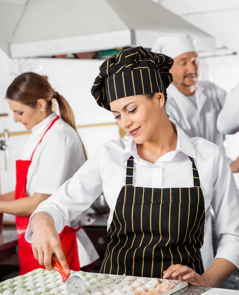 Kvinnliga kock skärande Ravioli Pasta med kollegor i bakgrunden — Stockfoto