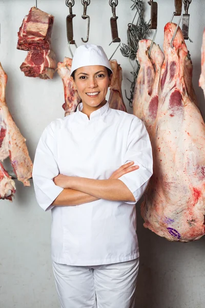 Macellaio in piedi contro la carne appesa in macelleria — Foto Stock