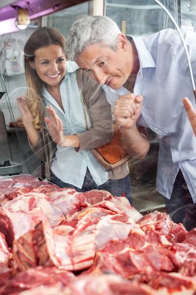 Paar betrachtet Fleisch durch Schrank in Metzgerei — Stockfoto