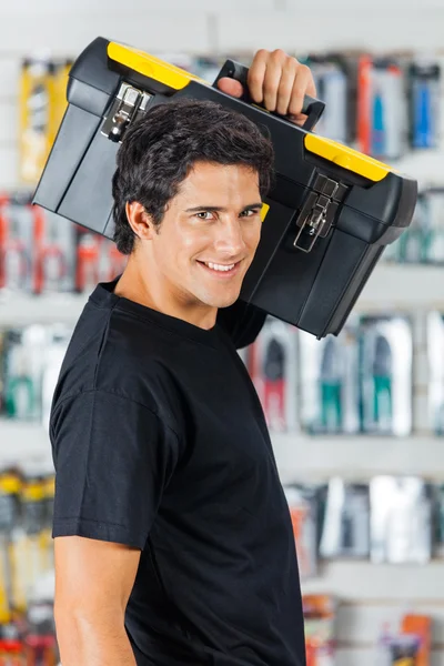 Zelfverzekerde Man uitvoering Toolbox op schouder In winkel — Stockfoto