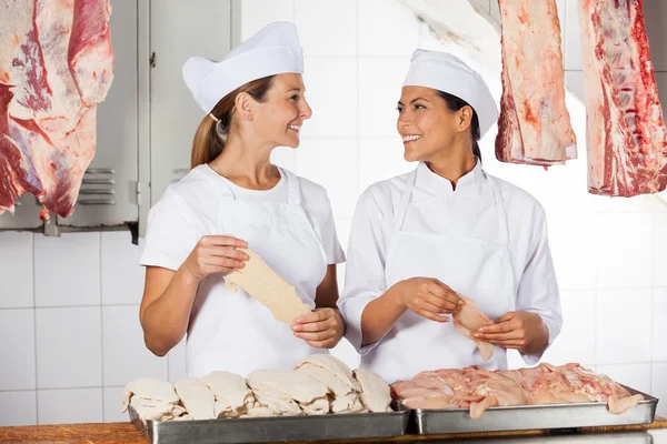 Carniceiros fêmeas segurando carne crua no balcão — Fotografia de Stock