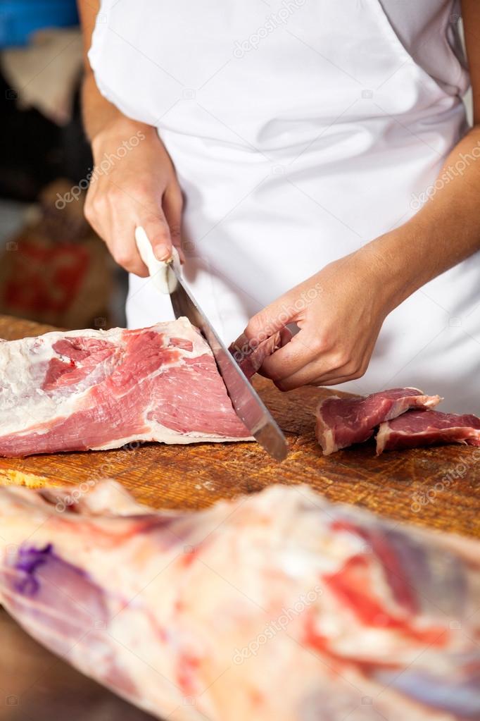 Female Butcher Cutting Raw Meat At Counter