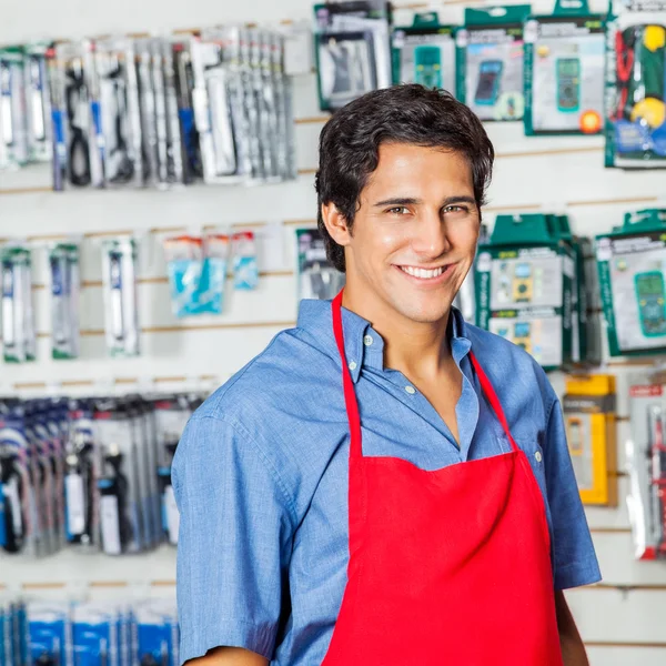 Trabalhador bonito em avental vermelho sorrindo na loja de ferragens — Fotografia de Stock