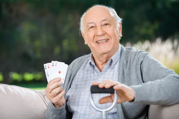 Anziano uomo holding quattro assi mentre seduta su divano — Foto Stock