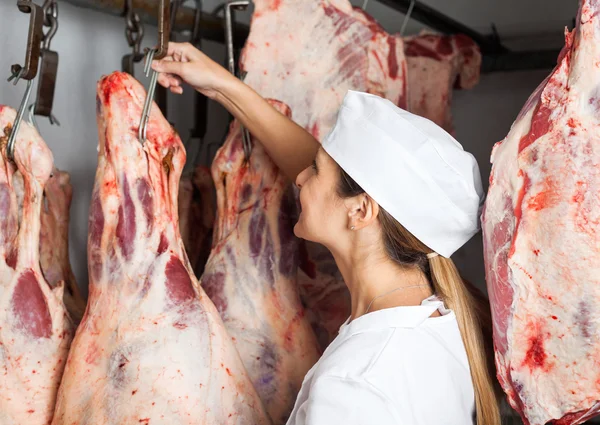 Vrouwelijke slager vlees In slagerij opknoping — Stockfoto