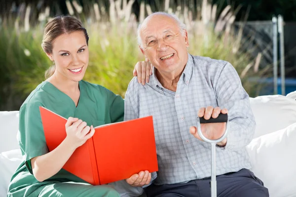 Lächelnde Krankenschwester und älterer Mann mit Buch — Stockfoto