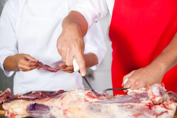 Slaktaren styckning av kött av kollega vid disken — Stockfoto