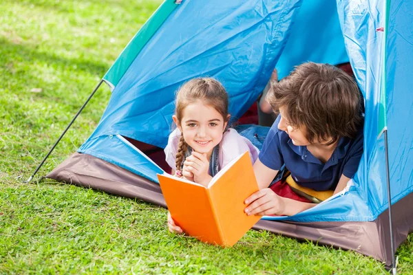 Gelukkig meisje met broer leesboek In Tent — Stockfoto